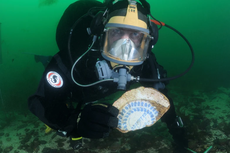 a person in black and yellow scuba suit and helmet is holding an item in his right hand