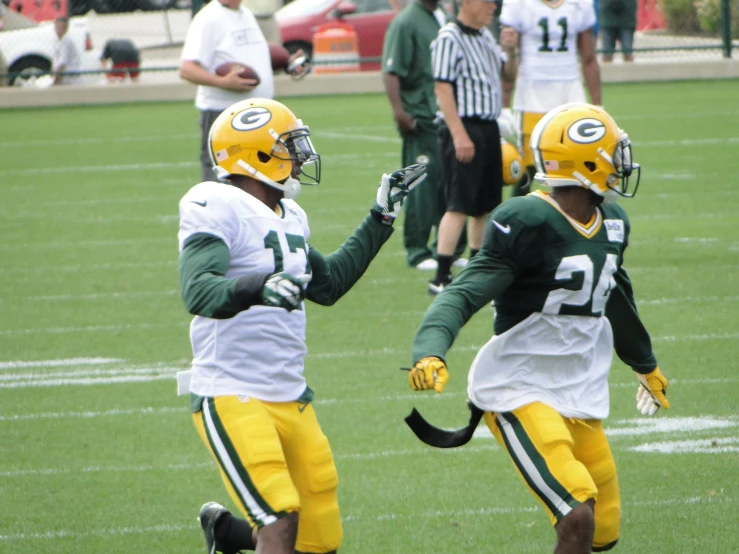 two green bay packers players holding hands and wearing green, white and yellow uniforms