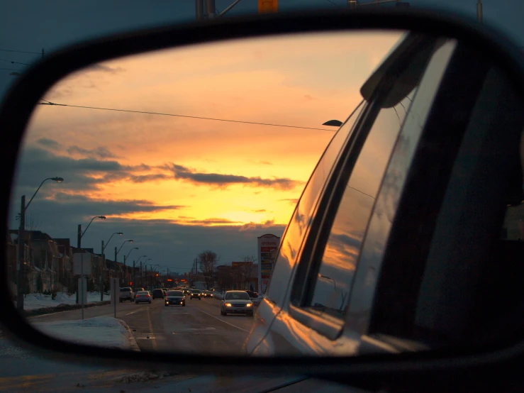 the cars are driving on the road as the sun sets in the mirror