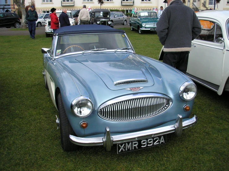 there are a few people in the yard viewing vintage cars