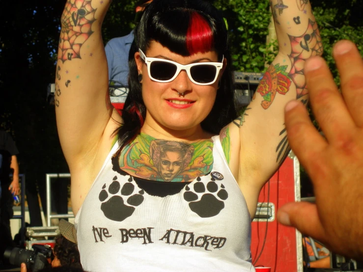 a woman with tattoos and sunglasses holds up her hands