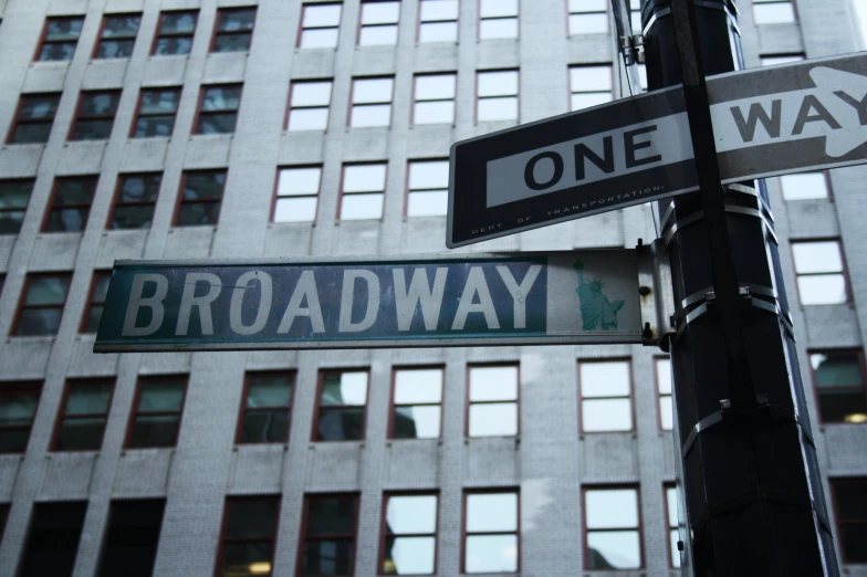 a one way sign at the corner of broadway and madison