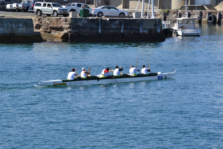 four people in white jackets are rowing a long boat down the water