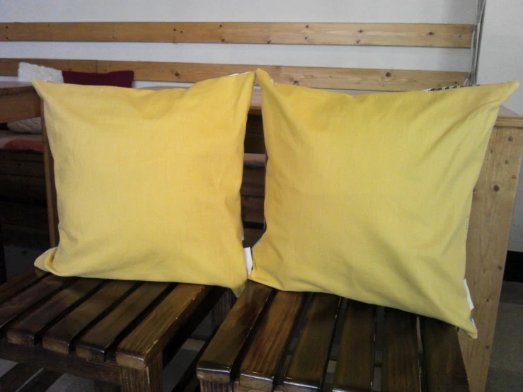 two yellow pillows on wooden benches in front of a white wall