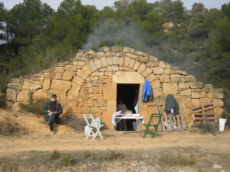 man sitting outside of his old fashioned stone hut