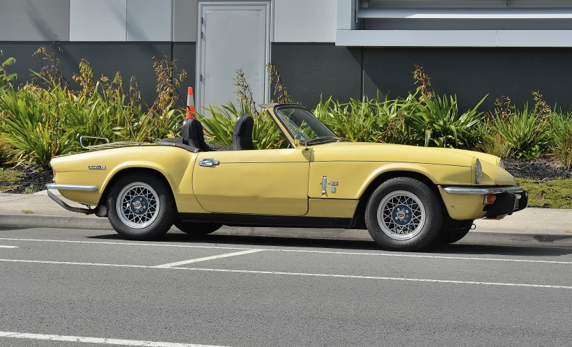 a yellow convertible car on street next to wall