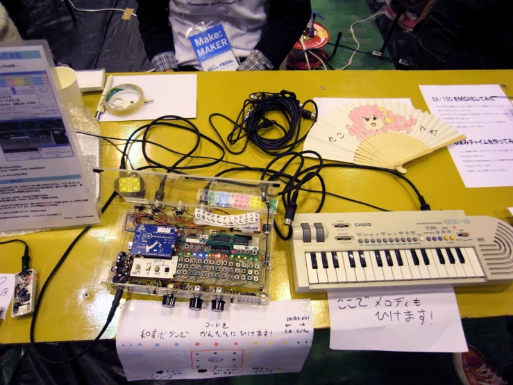 the electronic keyboard is on a yellow table next to paper, cards and wires