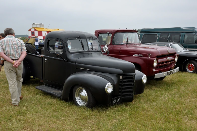 the men are standing outside by many classic trucks