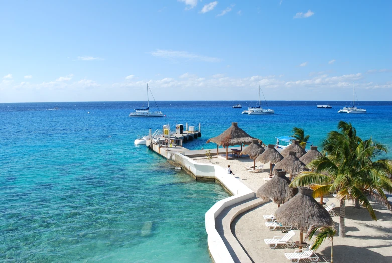 many boats on the blue water near some huts