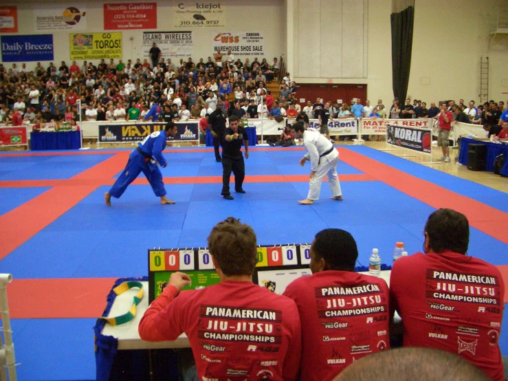 a group of people sitting on a court watching two men perform karate