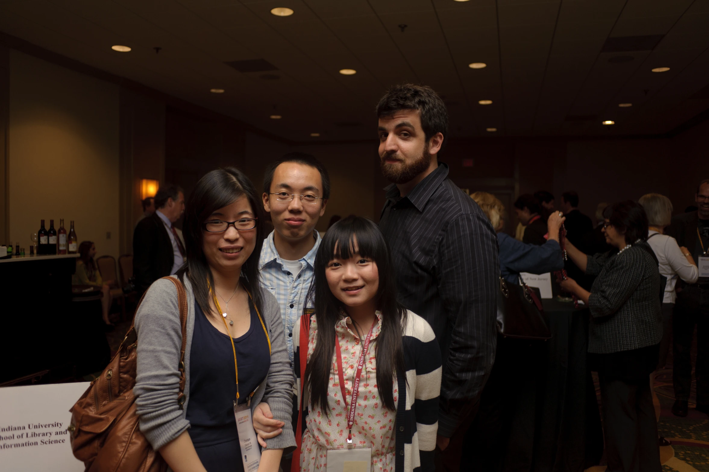 four people pose in front of a room with many other guests