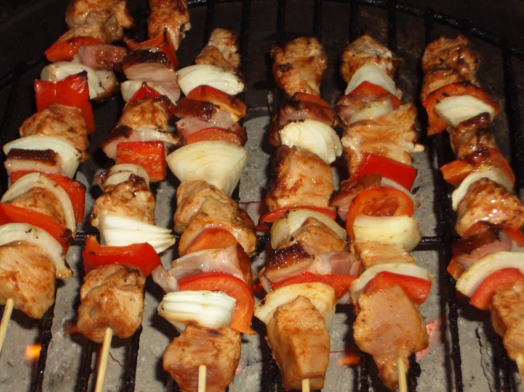 a bbq with skewered chicken, tomatoes and onions on a stick