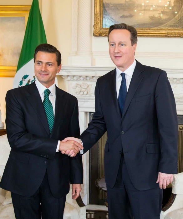 two men in business suits standing in front of the fireplace