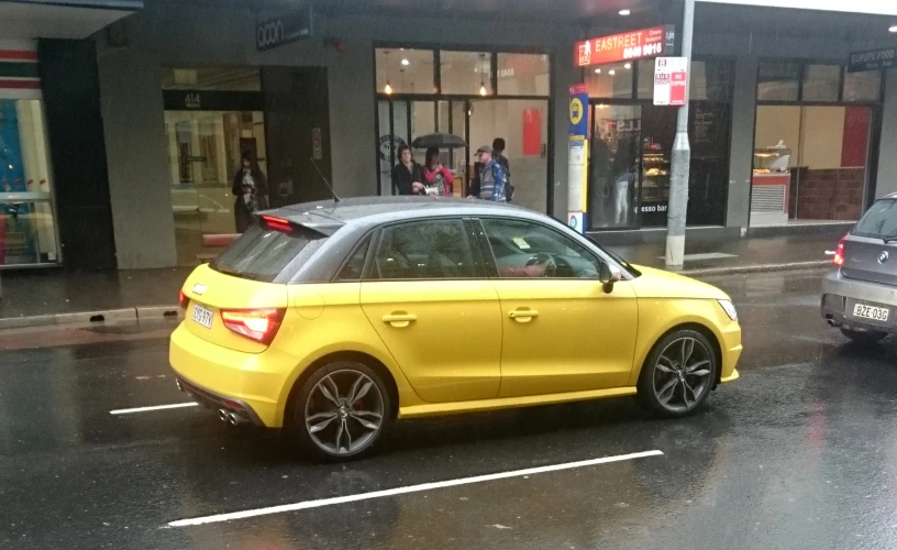 a yellow car in front of a store with people walking by