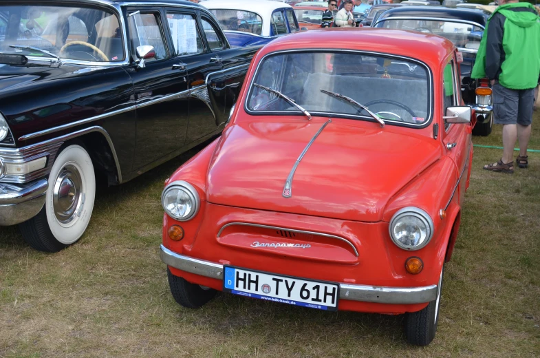 a red car sits on the grass with other old vehicles around it