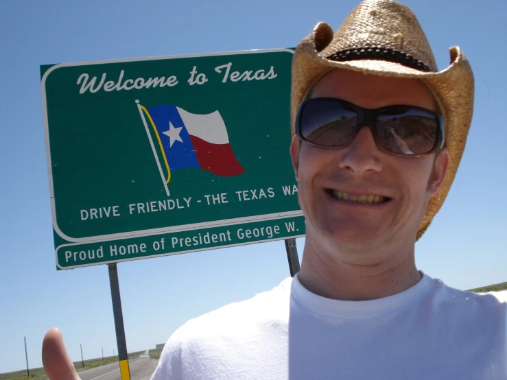man in cowboy hat with sign saying drive friendly - the texas way
