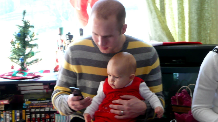 a man holds his little baby as he looks at his phone