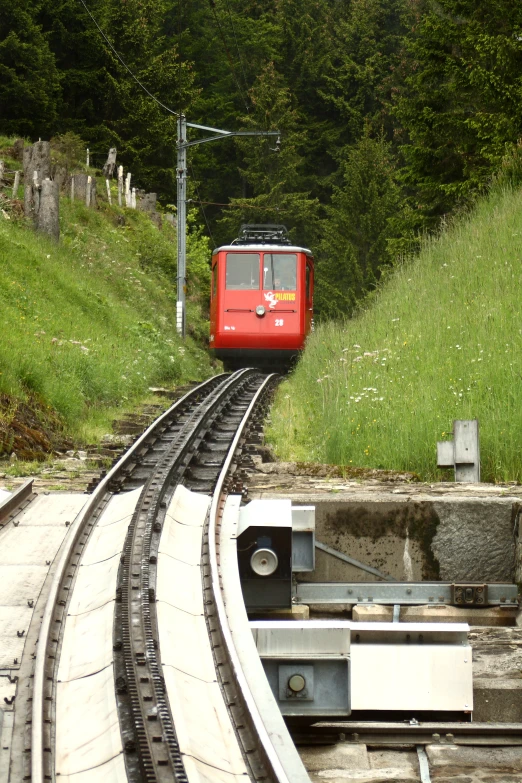 a red train traveling down the tracks with grass on both sides