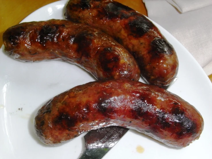 three grilled sausages on a plate with  sauce