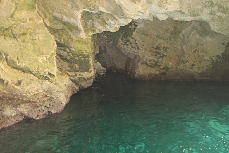 there is a small cave with a turquoise water below it