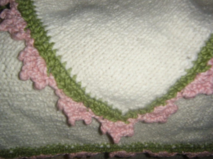 a pink and green knitted blanket sitting next to a white wall