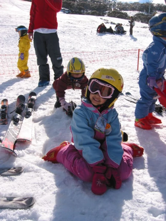 a girl is kneeling on the snow on skis with other children