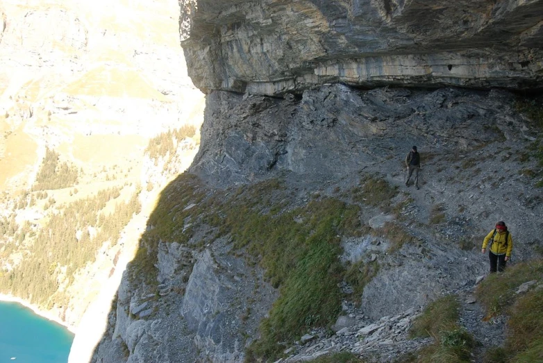 a man walks along side of a cliff next to blue water