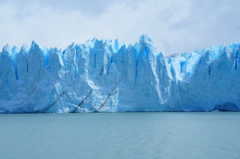 some people stand near an ice wall while a boat approaches