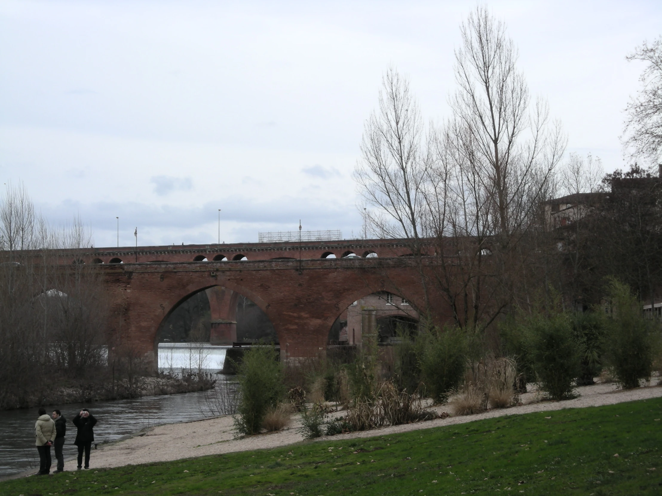 two people in black walking past a bridge and water