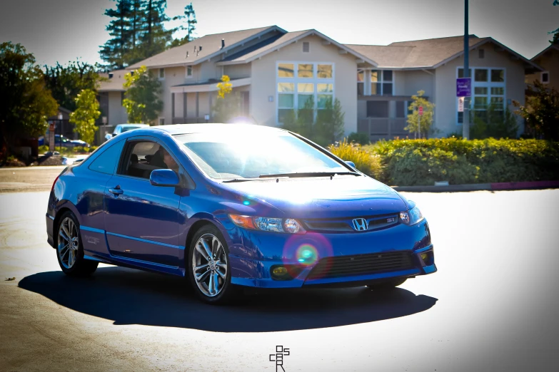 a blue sedan parked in a parking lot with houses in the background