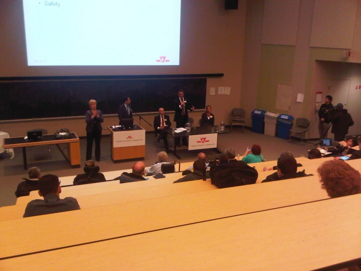 a group of people sit on benches while a man stands at the front of a lecture hall