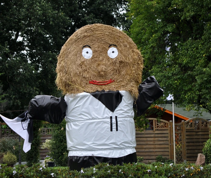 a large hay bale monster stands in front of trees
