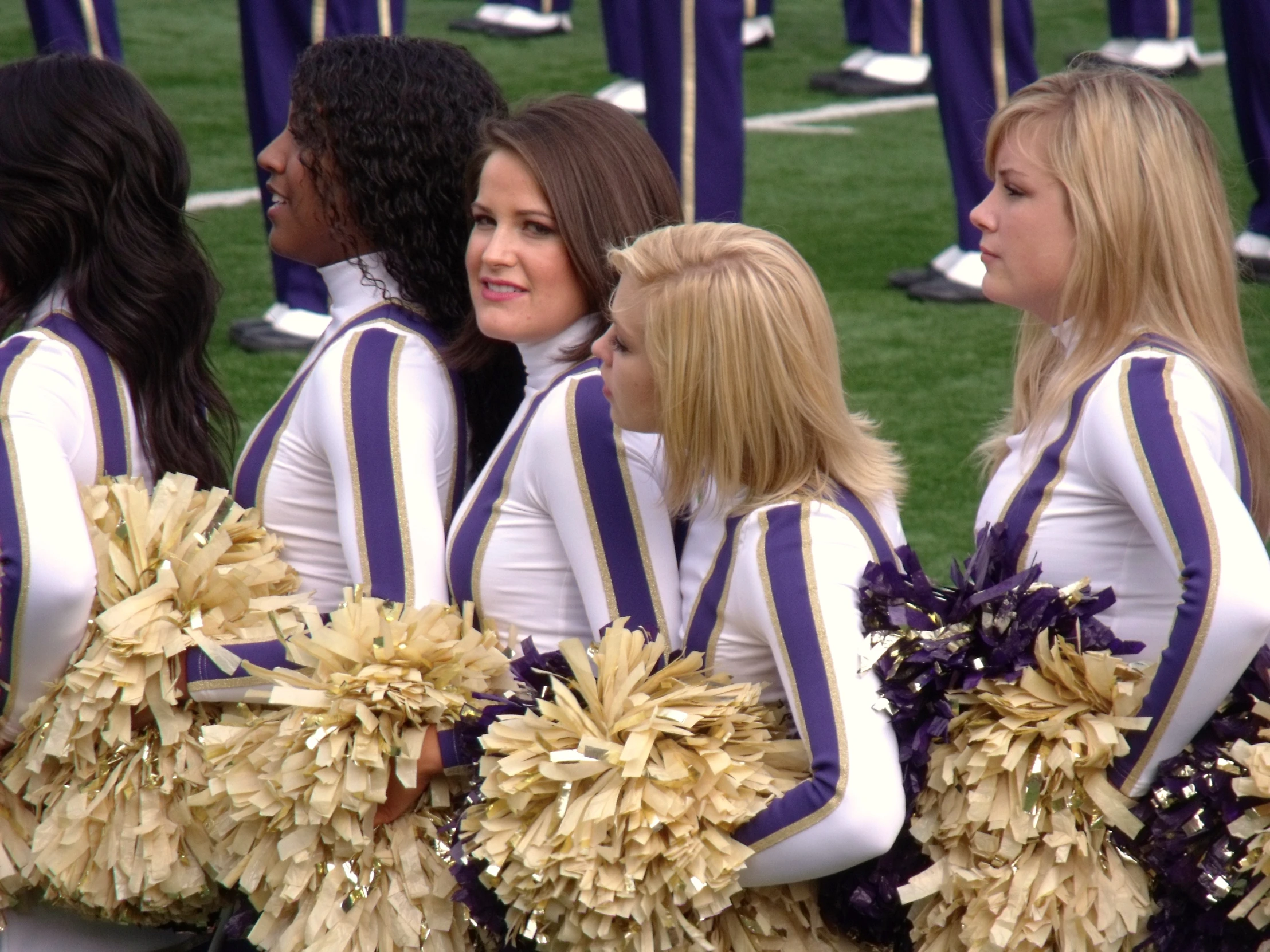 several female cheerleaders in uniforms sit together on the sidelines