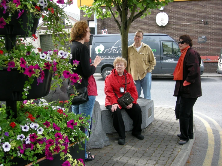 several people standing and sitting around some flowers