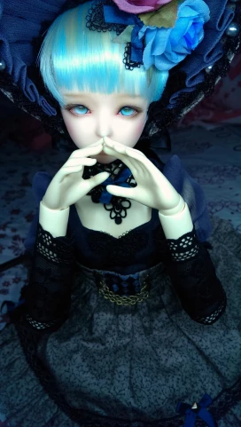 a doll dressed as a girl, sitting and holding her hands in front of her mouth