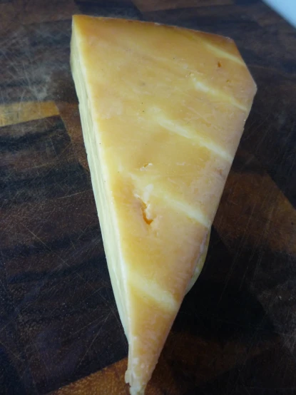 a single wedge of cheese sitting on top of a wooden  board