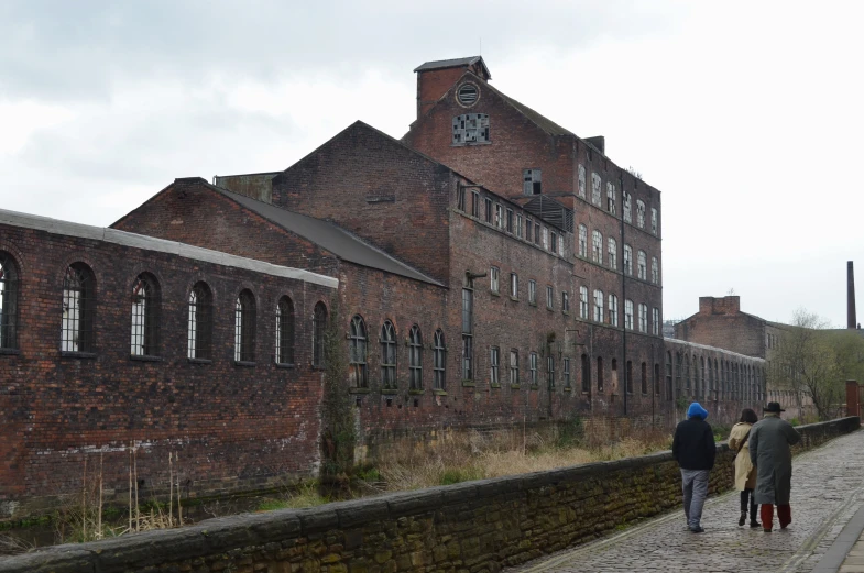 a group of people walk past an old brick building