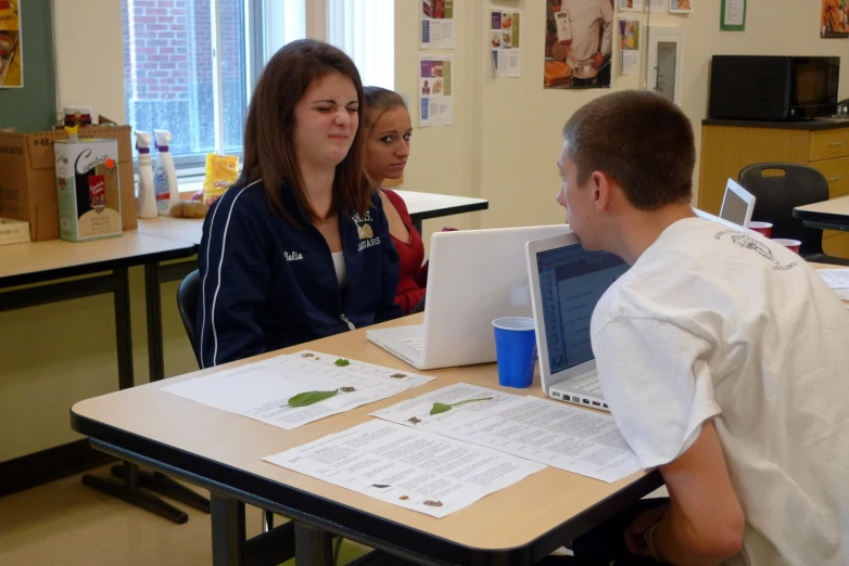 three students work on laptops in a classroom