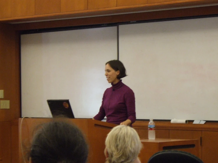 a woman standing at a podium next to a white board