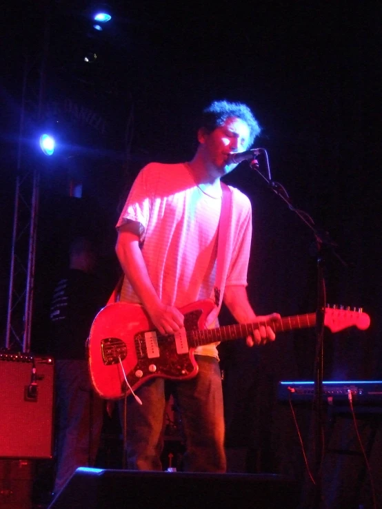 the man stands in front of his microphone, and plays the guitar