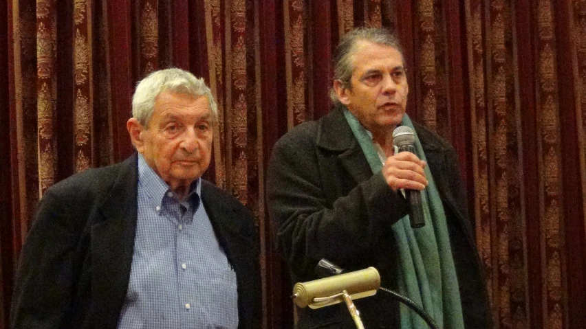 two men sitting at a table and one man is holding a microphone