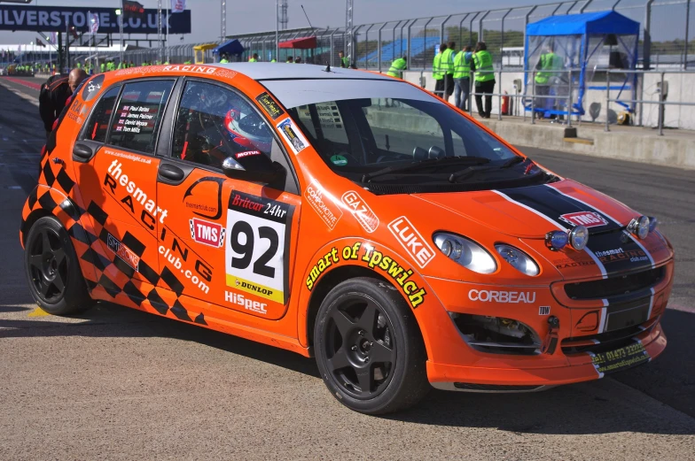 an orange and black car with some people watching