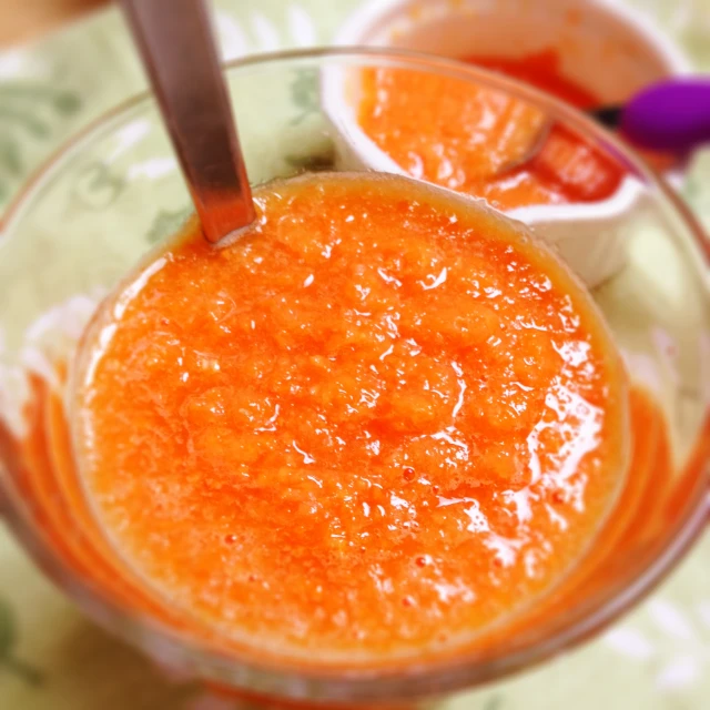 two bowls of orange liquid with spoons next to each other