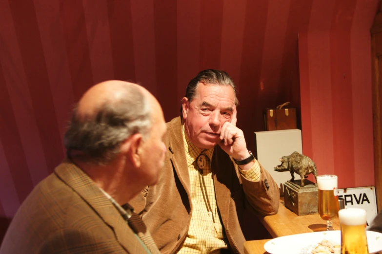 a man sitting at a bar next to another man with glasses