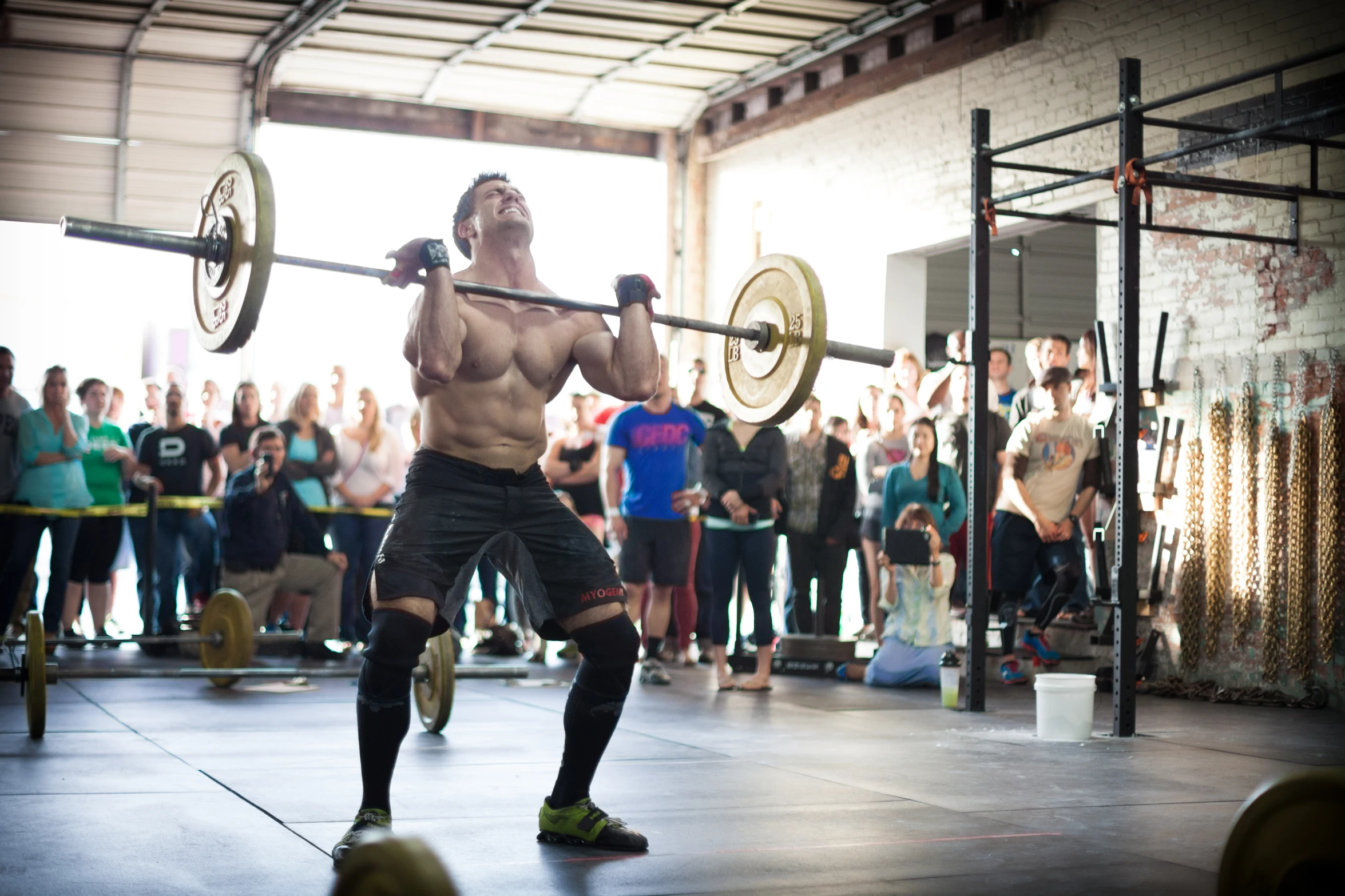 a man holding a weight bar above his head with people behind him