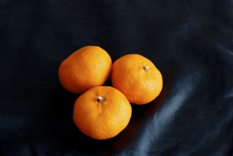 three oranges laying side by side on a black cloth