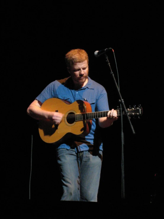 a man standing behind a microphone playing an acoustic guitar