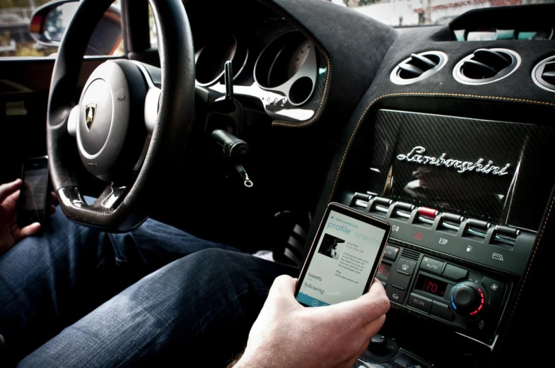 a man sitting in a car next to his steering wheel and holding a cell phone