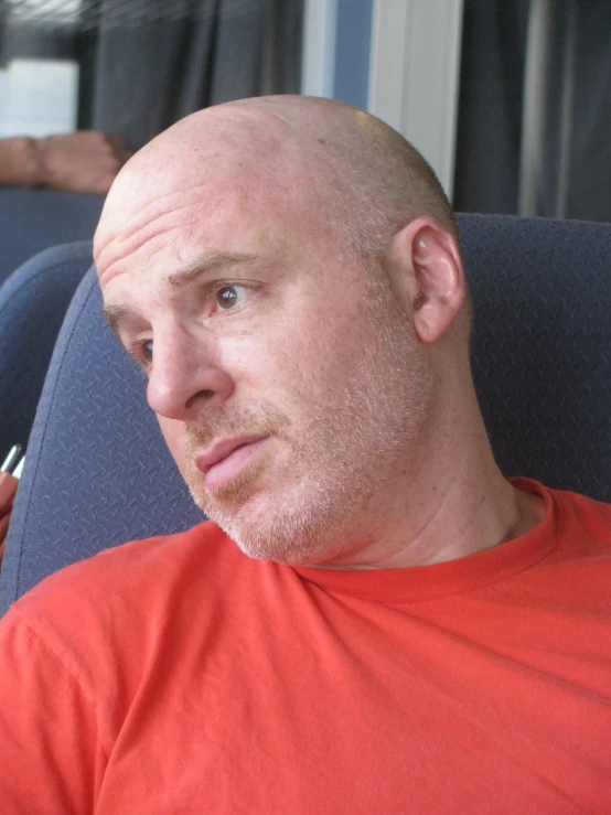 a bald man in an orange shirt with a pen