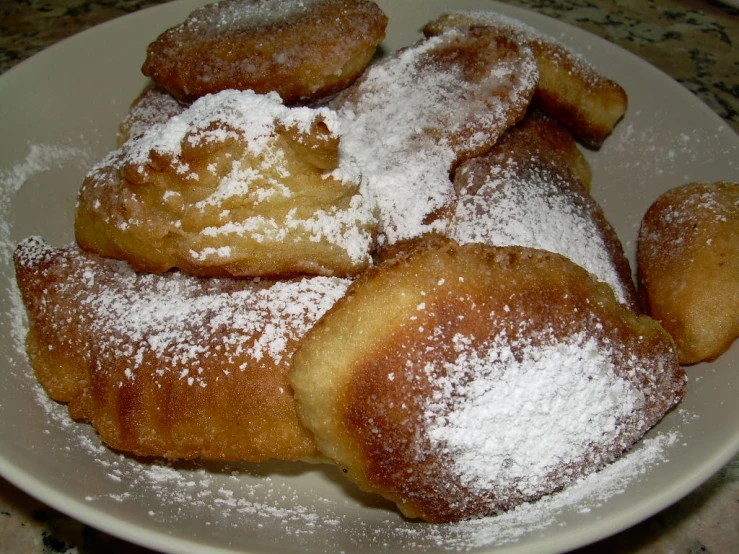 a white plate with doughnuts dusted with sugar